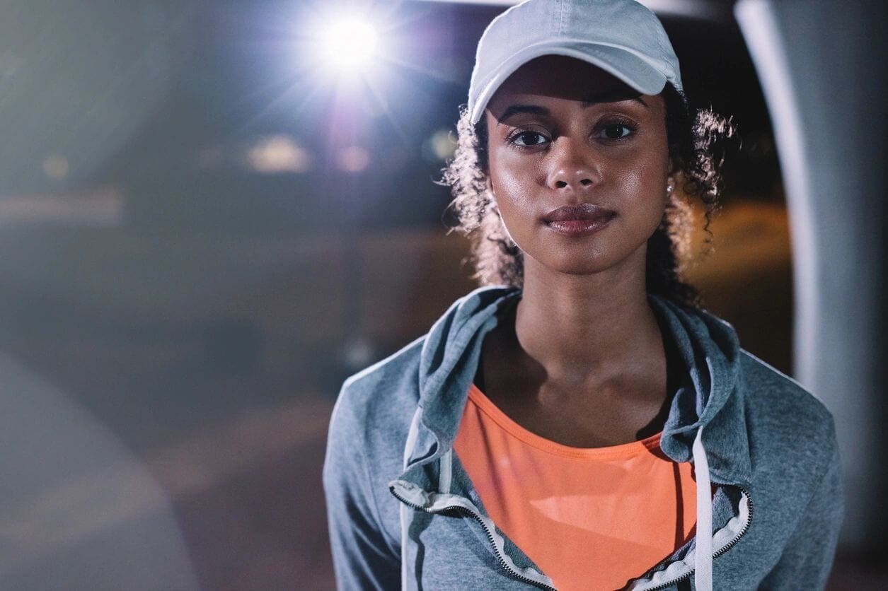 A woman wearing an orange shirt and white hat.