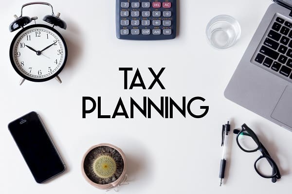 Tax Planning words written on white table with clock, smartphone, calculator, pen, cactus, glass and laptop Tax Planning words written on white table with clock, smartphone, calculator, pen, cactus, glass and laptop