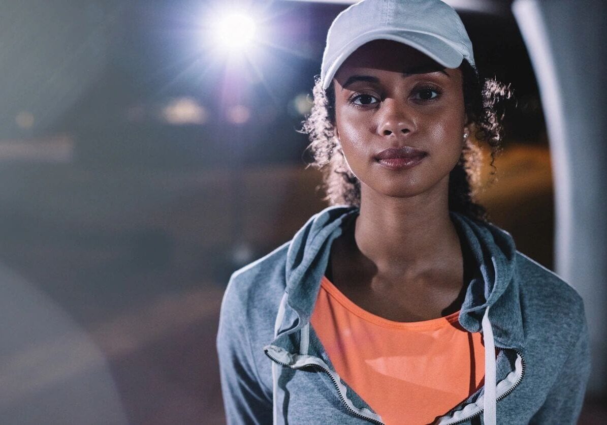 A woman wearing an orange shirt and white hat.